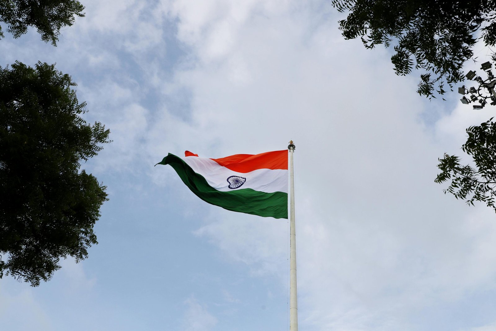 Low angle shot of the Indian national flag on a flagpole with a clear blue sky.