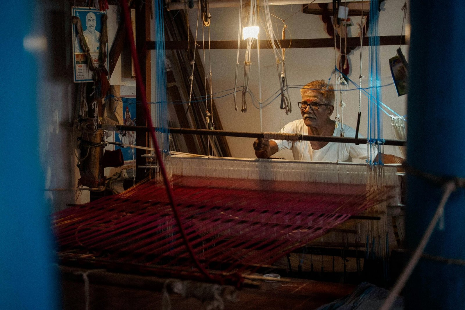 Elderly man weaving traditional Indian textiles indoors at a loom.